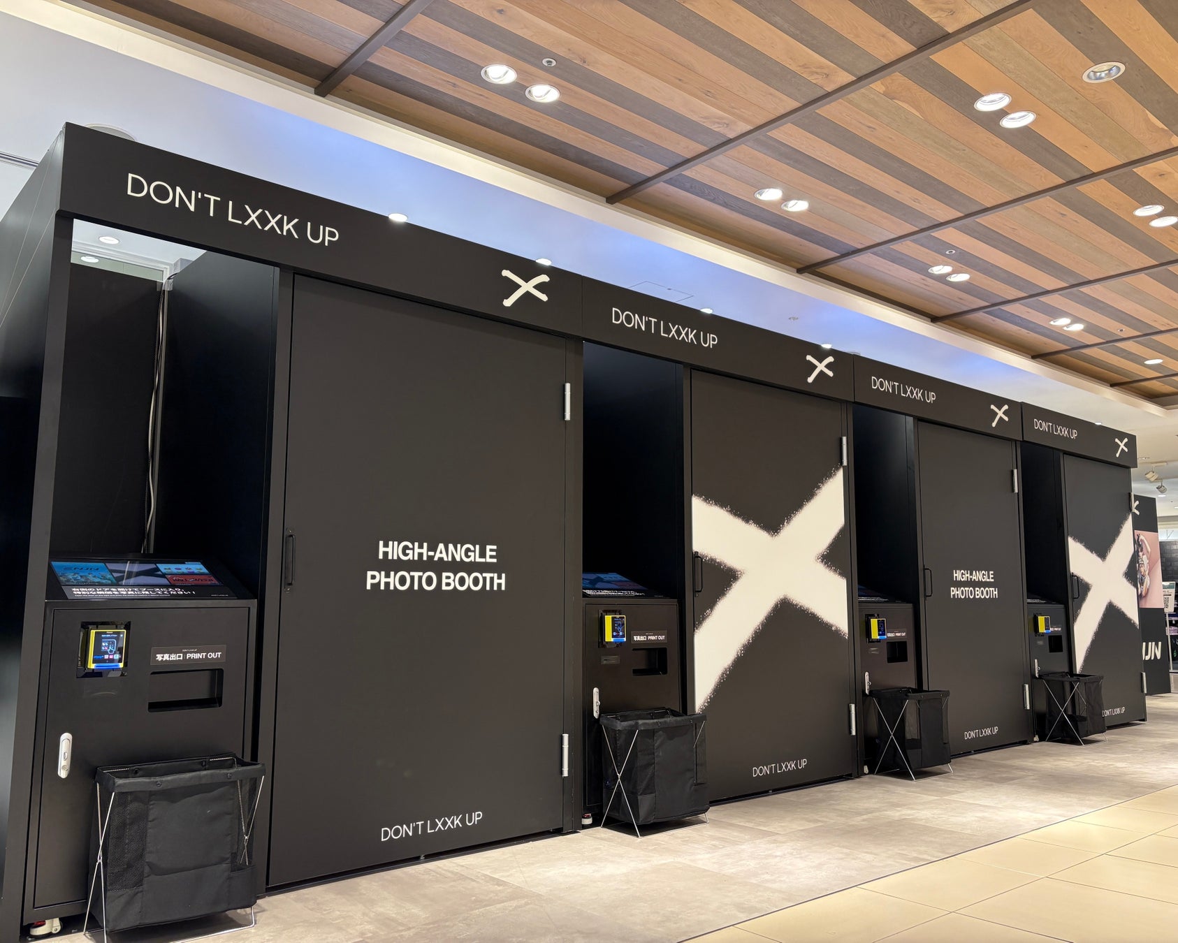 黒い「DON’T LXXK UP」の撮影ブースが屋内に並ぶ。扉には「HIGH-ANGLE PHOTO BOOTH」と白いX形の図柄がある。