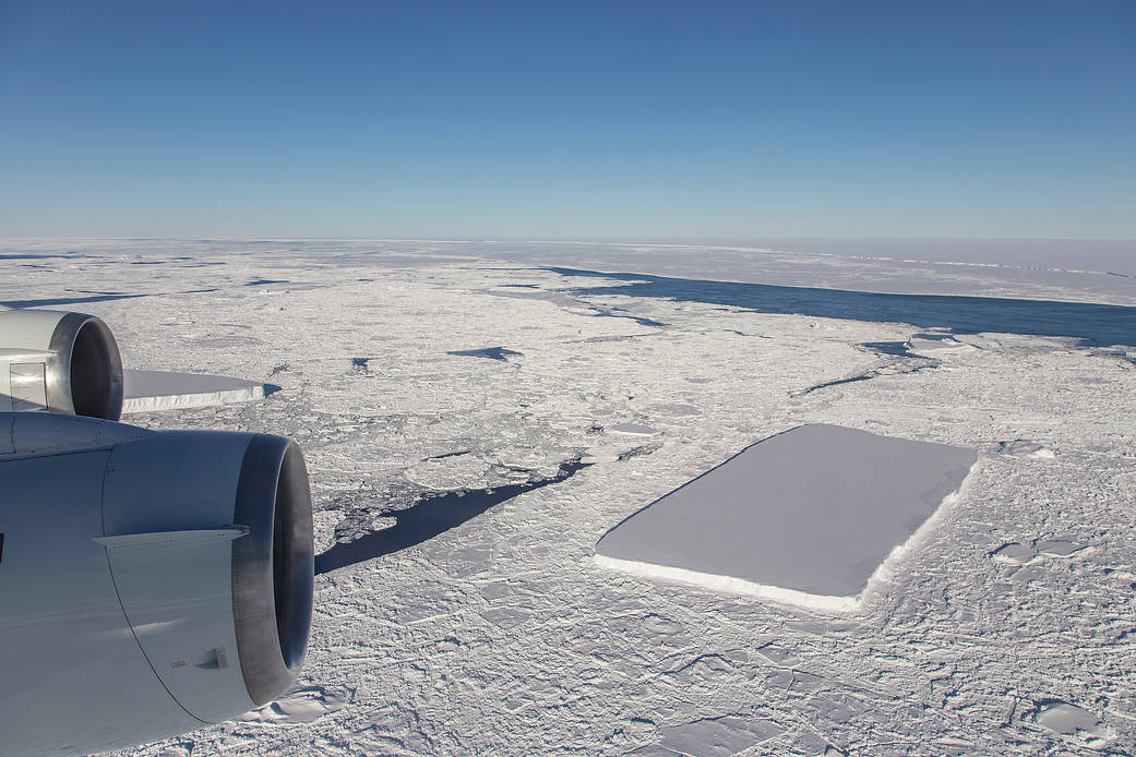 航空機のエンジン越しに見える氷山の端と、手前の平らで角ばった別の氷山