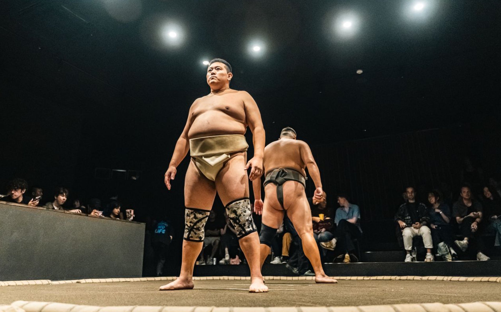 土俵上のまわし姿の2人と周囲の観客。主催者の開店告知掲載画像。